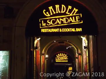 Złoty podświetlany szyld Garden le Scandale w łuku bramy